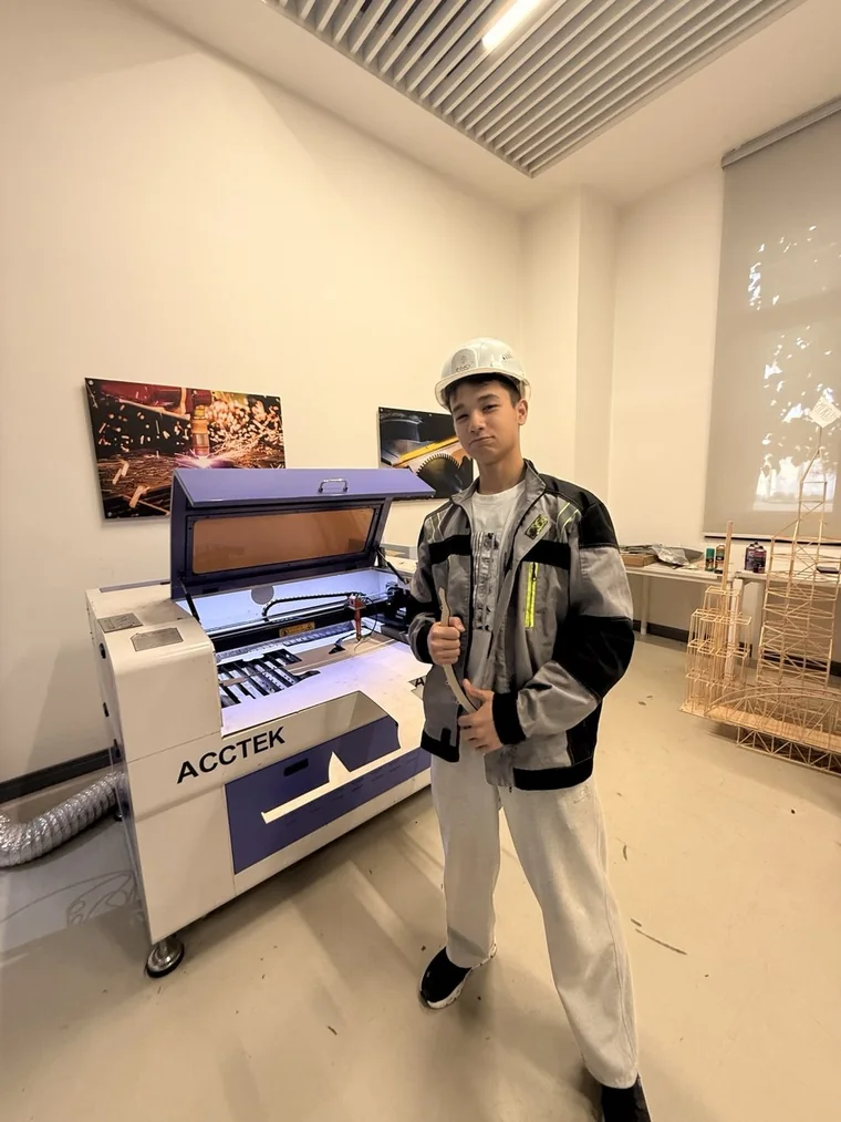 Me in a hard hat and work jacket, giving a thumbs up next to a laser cutter